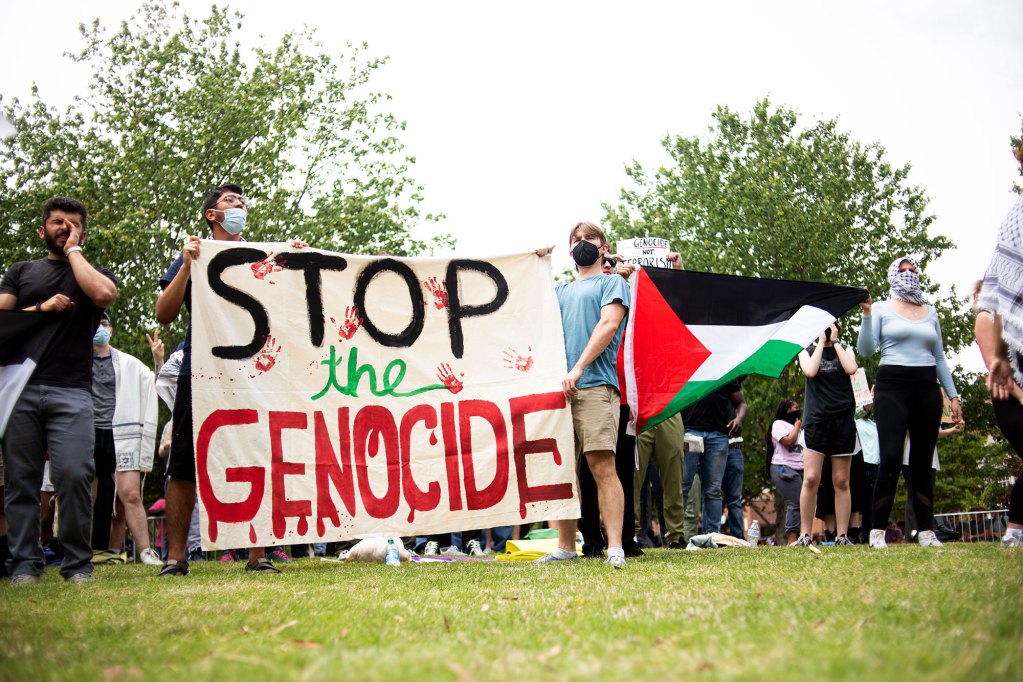 Pro-Palestine protesters hold a "Stop the Genocide" sgin and a Palestinian flag